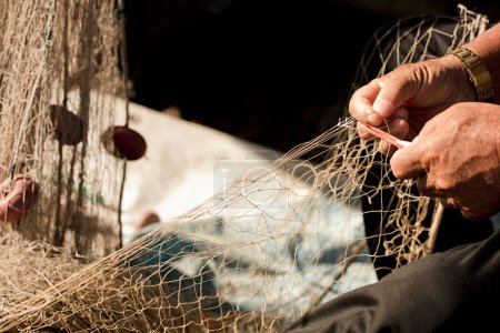 Foto de Red de pesca en manos del pescador, con aguja e hilo, agarra la red con los dedos de los pies - Imagen libre de derechos