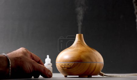 Foto de Wooden air freshener with steam of natural essences, man's hand with dispenser, gray background - Imagen libre de derechos