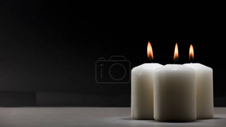 drei brennende Kerzen auf weißem Tisch mit schwarzem Hintergrund, Platz für Text