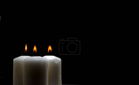 drei brennende Kerzen auf weißem Tisch mit schwarzem Hintergrund, Platz für Text