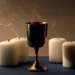 Golden Christian chalice with 4 extinguished candles with smoke, brown background