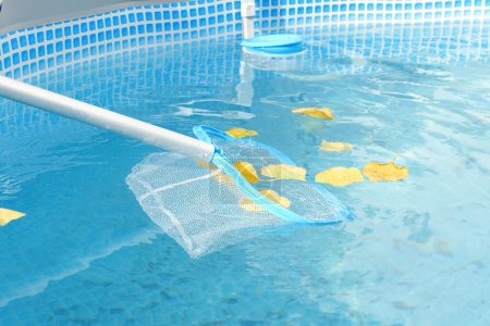 Foto de Limpieza de una piscina con un skimmer de malla. La larga red limpia las hojas de color de la superficie del agua. - Imagen libre de derechos