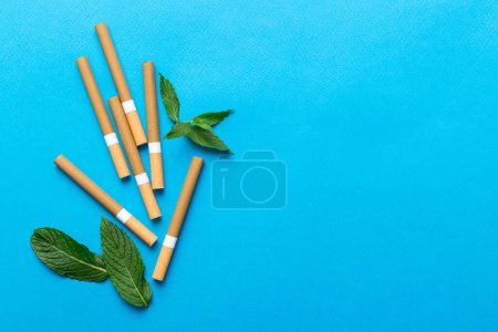 Foto de Cigarrillos de mentol y hojas de menta fresca sobre fondo de color, muchos cigarrillos apilados juntos vista superior plana. - Imagen libre de derechos