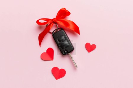 Car key with a red bow and a heart on Colored table. Giving present or gift for valentine day or christmas, Top view with copy space.