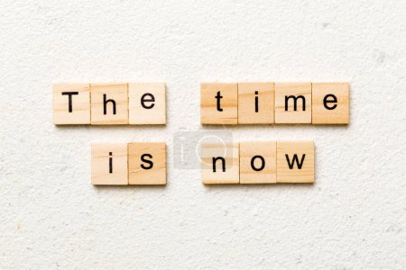 the time is now word written on wood block. the time is now text on table, concept.