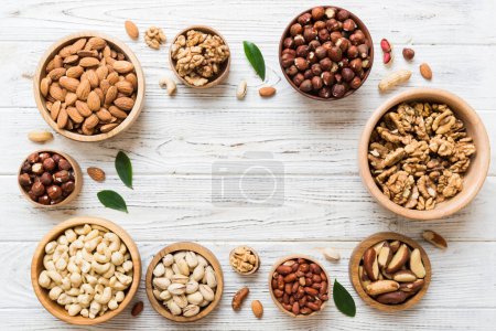 Téléchargez les photos : Mixed nuts in wooden bowl. Mix of various nuts on colored background. pistachios, cashews, walnuts, hazelnuts, peanuts and brazil nuts. - en image libre de droit