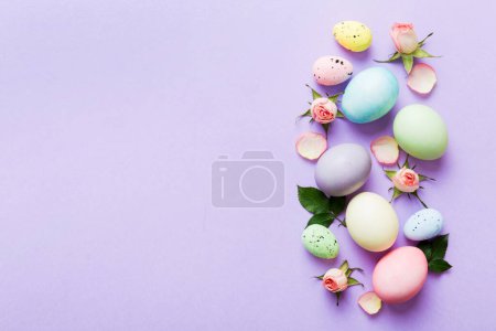 Feliz Pascua. Huevos de Pascua sobre mesa de colores con rosas amarillas. Huevos coloridos teñidos naturales vista superior de fondo con espacio de copia.