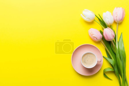 Fondo de primavera con flores, una taza de café y un ramo de tulipanes rosados y blancos sobre fondo de mesa de colores con lugar para el texto. Copiar vista superior del espacio.