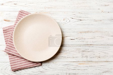 Draufsicht auf farbigem Hintergrund leerer runder weißer Teller auf Tischdecke für Lebensmittel. Leere Schale auf Serviette mit Platz für Ihr Design.