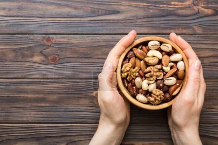 Photo for Woman hands holding a wooden bowl with mixed nuts Walnut, pistachios, almonds, hazelnuts and cashews. Healthy food and snack. Vegetarian snacks of different nuts. - Royalty Free Image