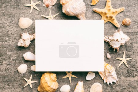 Foto de Summer time concept with blank greeting card and blank white paper on colored background. Seashells from ocean shore in the shape of frame separated with space for text top view. - Imagen libre de derechos