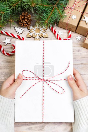 Photo for Top view of christmas letter in hand. Close up of hands holding empty wishlist on wooden table with xmas decoration. - Royalty Free Image