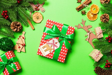 Photo for Top view of female hands holding a Christmas present on festive green background. Fir tree and holiday decorations. New Year holiday concept. - Royalty Free Image