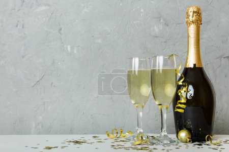 Champagne bottle with confetti, glasses and christmas decor on colored holiday background. Flat lay New Year decorations.