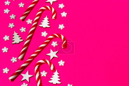 Weihnachtsbonbons lagen gleichmäßig hintereinander auf rosa Hintergrund mit dekorativer Schneeflocke und Stern. flache Lage- und Draufsicht.