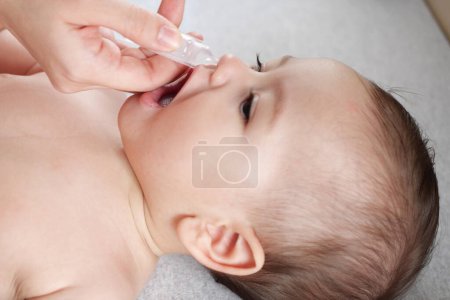 Téléchargez les photos : Mère goutte des gouttes nasales pour son fils. Concept de soins de santé bébé vue du dessus. - en image libre de droit