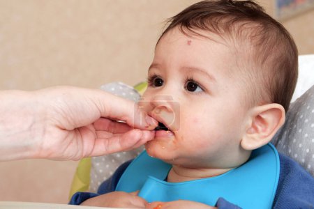 Portrait d'un petit garçon mangeant de la nourriture. Bébé avec une cuillère dans la chaise d'alimentation. Bébé mignon manger le premier repas.