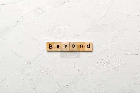 BEYOND Wort auf Holzblock geschrieben. BEYOND-Text auf Zementtisch für Ihre Gestaltung, Ihr Konzept.