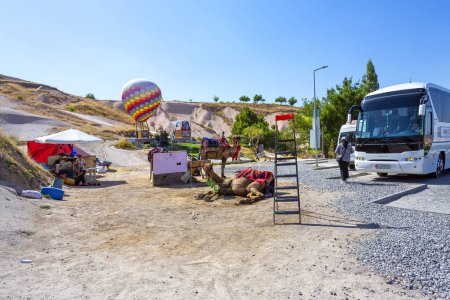 Foto de GOREME, TURQUÍA 2023, 07 de agosto: Foto tomada frente a la entrada del pueblo de Uchisar, autobús turístico, camello y globo aerostático. - Imagen libre de derechos