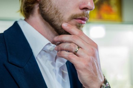 Photo for Handsome man in a stylish fashionable suit holds chin at a jewelry store. A male model with a ring on his finger holds face in close-up at a diamond shop - Royalty Free Image