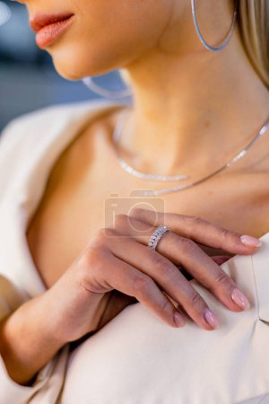 Burn an elegant diamond ring on the female finger, necklace and large round earrings. Girl stands in a jewerly store. Love and wedding concept. Soft and selective focus