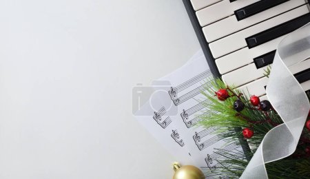 Konzeptionelles Detail der Weihnachtsaufführung von Klavier mit Instrument und Noten auf weißem Tisch und Weihnachtsdekoration. Ansicht von oben.