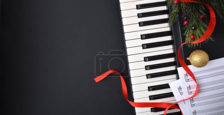 Fondo de actuación navideña de piano con instrumento y partitura en mesa negra y decoración navideña...