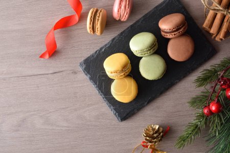 Téléchargez les photos : Macarons français de différentes saveurs sur une plaque d'ardoise sur une table en bois avec des décorations de Noël. Vue du dessus. - en image libre de droit