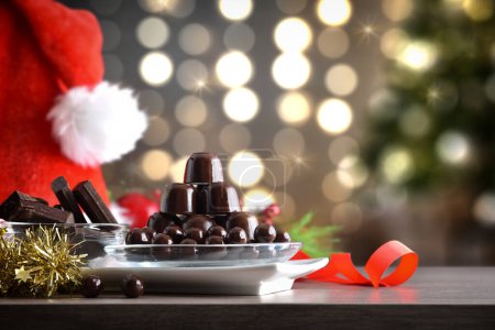 Téléchargez les photos : Assiette avec pile de chocolats et boules de chocolat noir sur table en bois avec décoration de Noël et fond de Noël avec lumières. Vue de face. - en image libre de droit