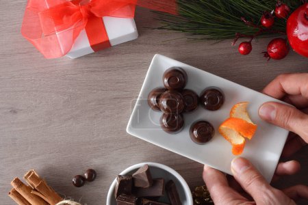 Téléchargez les photos : Assiette de service mains avec bonbons chocolat noir sur table en bois avec décoration de Noël. Vue du dessus. - en image libre de droit