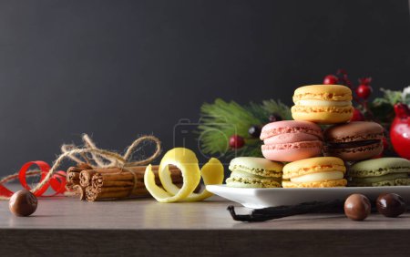 Téléchargez les photos : Empilement de différentes saveurs macarons français servis sur une assiette blanche sur une table en bois avec un fond sombre et un chapeau de Père Noël. Vue de face. - en image libre de droit