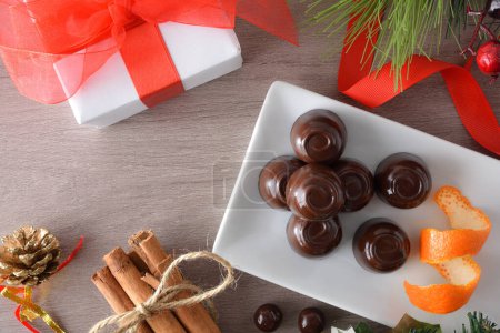 Téléchargez les photos : Bonbons au chocolat détail sur une plaque rectangulaire sur une table en bois avec des décorations de Noël. Vue du dessus. - en image libre de droit