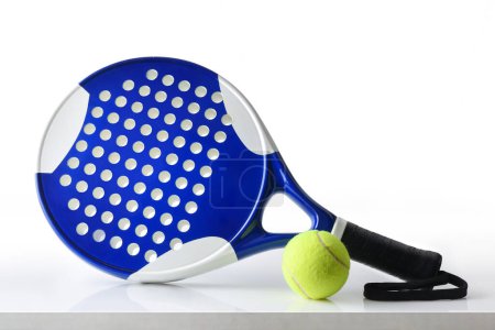 Foto de Padel racket and ball reflected on white table and white isolated background. Front view. - Imagen libre de derechos