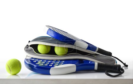 Foto de Paddle rackets equipment with case full of balls reflected on white table and white isolated background. Front view. - Imagen libre de derechos