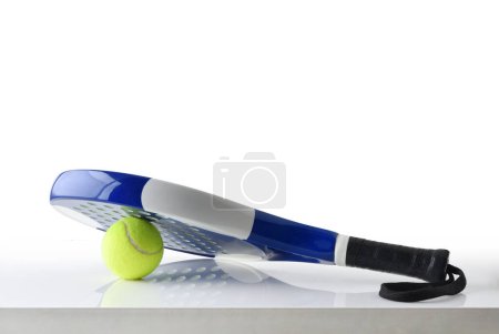 Foto de Padel racket on ball reflected on white table and white isolated background. Front view. - Imagen libre de derechos