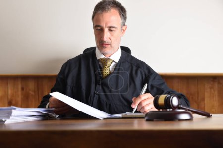 Photo for Judge sitting in an armchair reviewing the summary of a case on a wooden table. Front view - Royalty Free Image