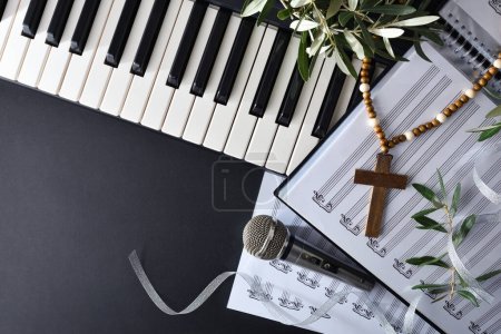 Téléchargez les photos : Musique religieuse avec piano et chœurs sur une table noire ornée de branches d'olivier et d'une croix chrétienne pour la fête du dimanche des Rameaux. Vue du dessus. - en image libre de droit