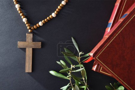 Foto de Trasfondo religioso pascual con símbolos como libros de cruz cristiana y ramas de olivo sobre mesa negra. Vista superior. - Imagen libre de derechos