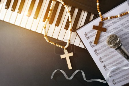 Musique religieuse avec piano et microphone sur dossier de partitions sur une table noire avec croix et éclat doré. Vue du dessus.