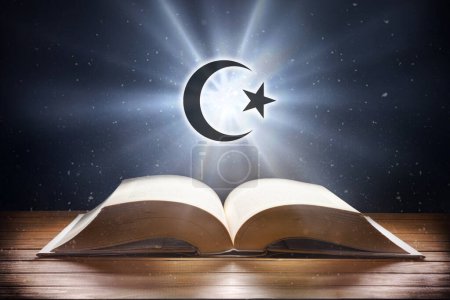 Foto de Libro abierto sobre mesa de madera y símbolo islámico con haz de luz con fondo oscuro. Vista frontal. - Imagen libre de derechos