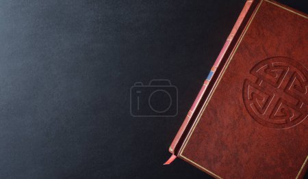 Foto de Libro de cultura y religión shenista con símbolo religioso grabado en la cubierta de cuero marrón sobre una mesa negra. Vista superior. - Imagen libre de derechos