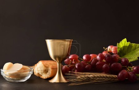 Hintergrund von Weinglas und Oblaten mit Brot und Deko-Trauben auf Tisch und schwarzem Hintergrund. Frontansicht.
