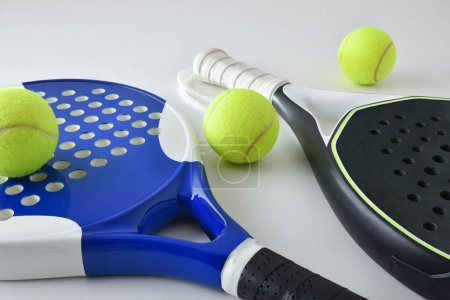 Background with two blue and black paddle rackets on a white table with balls. Elevated view.