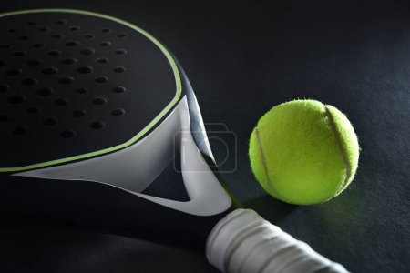 Detailed background of black and white padel racket and ball on black background. Elevated view.