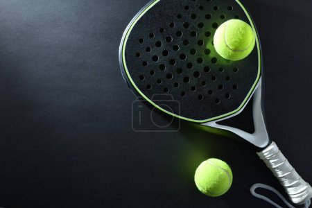 Hintergrund eines schwarz-weißen Paddle-Tennisschlägers und zwei Bälle auf einem schwarzen Tisch. Ansicht von oben.