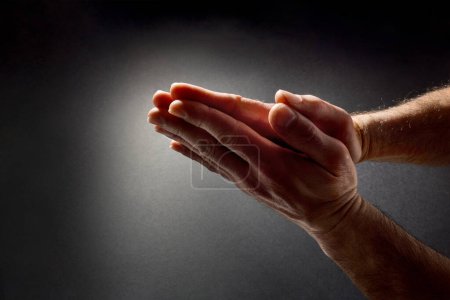 Foto de Hombre rezando con las manos con las palmas juntas en contraste con el haz de luz en el oscuro fondo del gradiente aislado. Vista superior. - Imagen libre de derechos