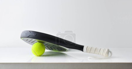 Foto de Dos raquetas de pádel blanco y negro que descansan sobre una pelota reflejadas sobre una mesa blanca y un fondo blanco aislado. Vista frontal. - Imagen libre de derechos