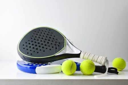 Foto de Dos raquetas de paddle azules y negras sobre mesa blanca con bolas y fondo blanco aislado. Vista frontal. - Imagen libre de derechos