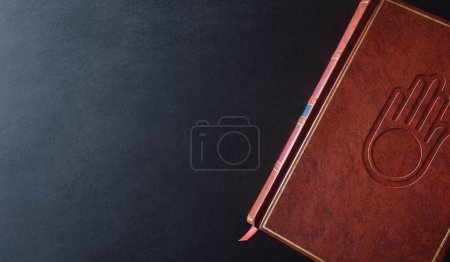 Téléchargez les photos : Livre de culture et de religion jaïn avec symbole religieux gravé sur la couverture en cuir marron sur une table noire. Vue du dessus. - en image libre de droit