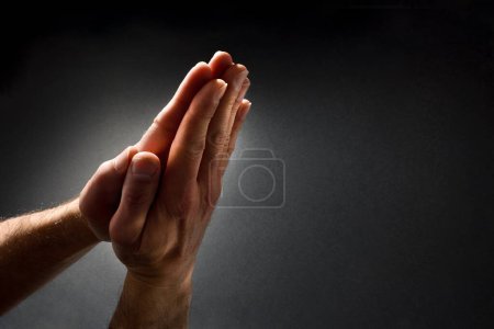 Foto de Hombre rezando con las manos con las palmas juntas en contraste con el haz de luz en el oscuro fondo del gradiente aislado. Vista superior elevada. - Imagen libre de derechos
